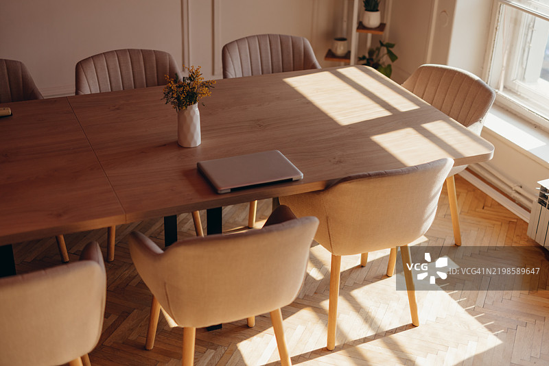 现代会议室，木桌、椅子和笔记本电脑沐浴在阳光下图片素材