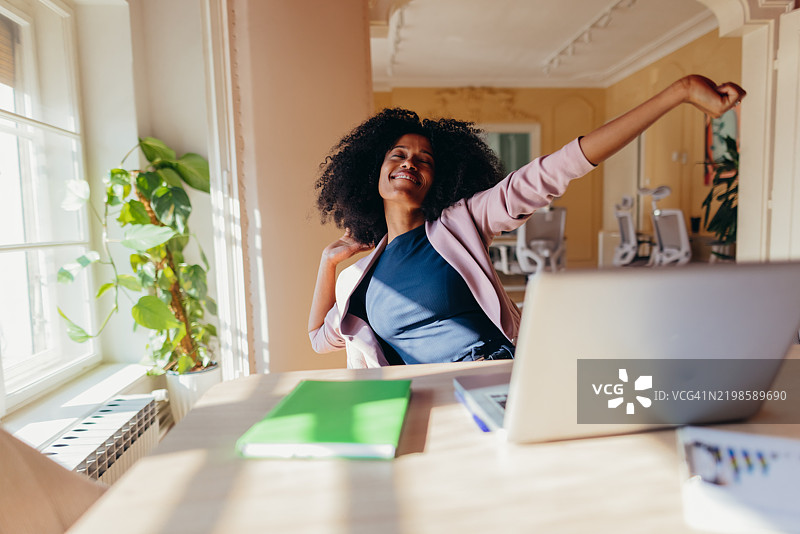 年轻女商人在完成工作后在桌子旁伸展身体图片素材