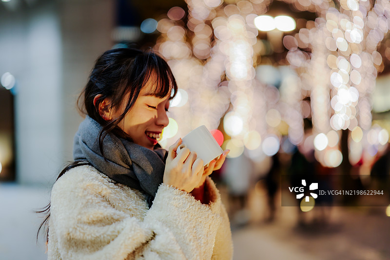 年轻美丽的女人在灯光璀璨的街道上喝咖啡图片素材