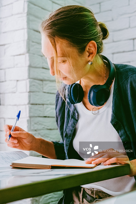 专注的女性在舒适的砖砌室内环境中戴着耳机学习。图片素材