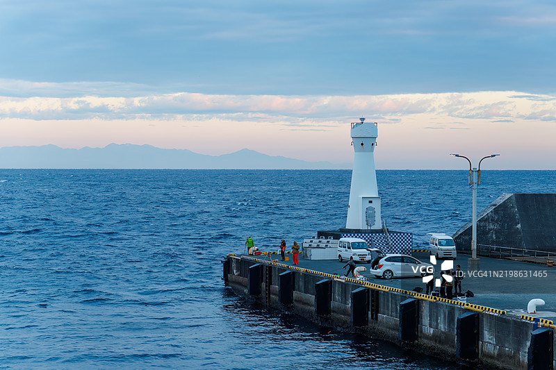 大岛的美丽冈田港的黎明。港口工作人员和其他人正在进行装载作业，游客正在登船，警察正在监控该地区。图片素材