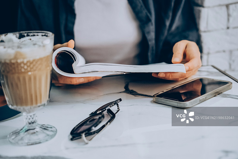 在大理石桌上享受放松的咖啡时光，旁边有杂志、智能手机和太阳镜。图片素材