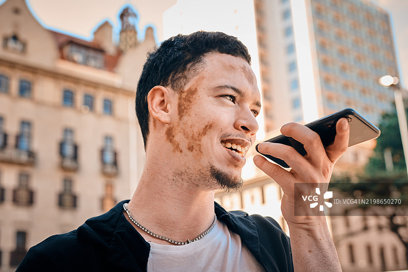 自信的白癜风男性在城市环境中使用智能手机交谈图片素材