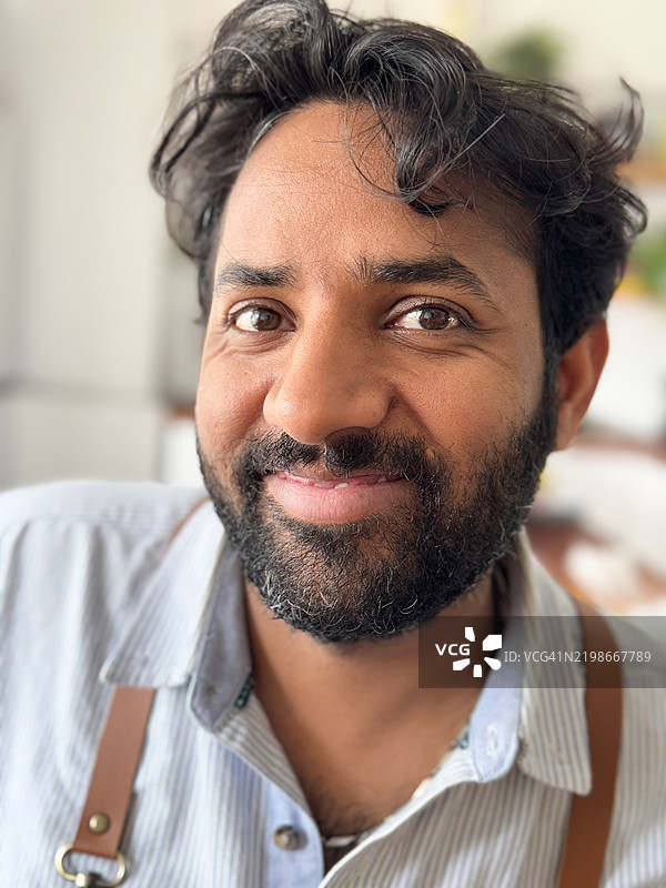 印度男子特写，留有胡须，穿着皮围裙，微笑着看向镜头，头部肖像，前景聚焦。图片素材
