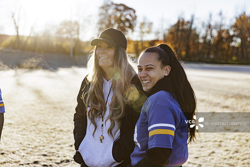 橄榄球运动员与女教练站在场上，目光投向远方。图片素材