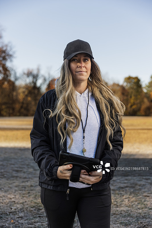 戴着帽子的女性教练在场地上站着，手持数字平板电脑的肖像图片素材