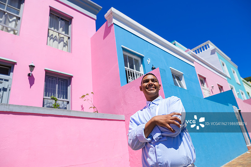 年轻男子在色彩斑斓的历史悠久的博卡普马来区粉色和蓝色房屋前摆姿势。图片素材