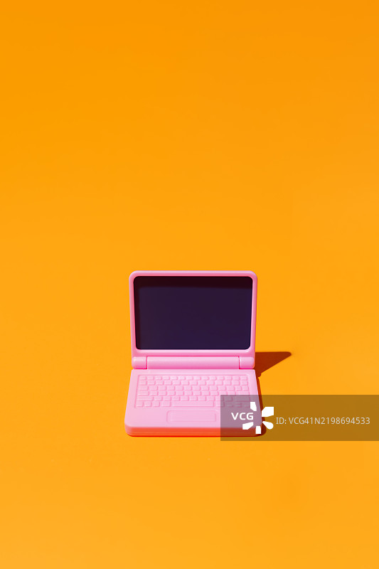 粉色笔记本电脑放在橙色背景上，屏幕为空白图片素材