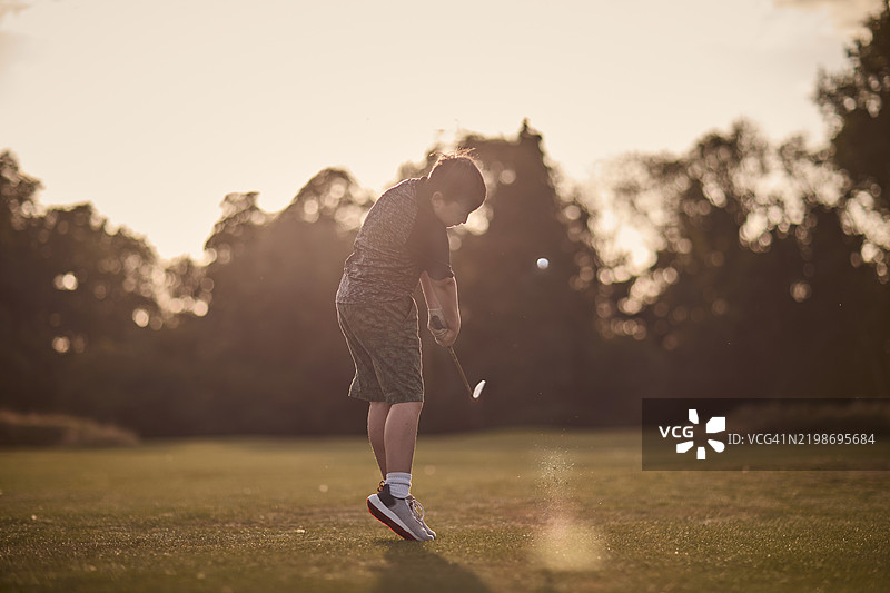 一位年轻的初级高尔夫球手在英国的风景如画的高尔夫球场上打球，正值夏末。图片素材