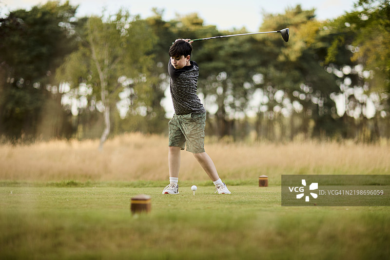 一位年轻的初级高尔夫球手在英国的风景如画的高尔夫球场上打球，正值夏末。图片素材
