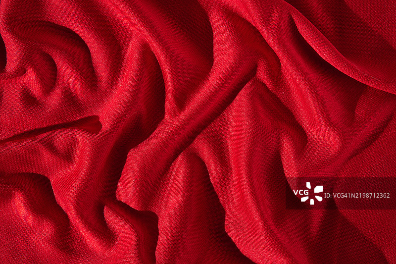 丰富的红色缎面纹理背景，带有波浪和褶皱。用于奢侈品展示的布料背景。平铺，特写。图片素材