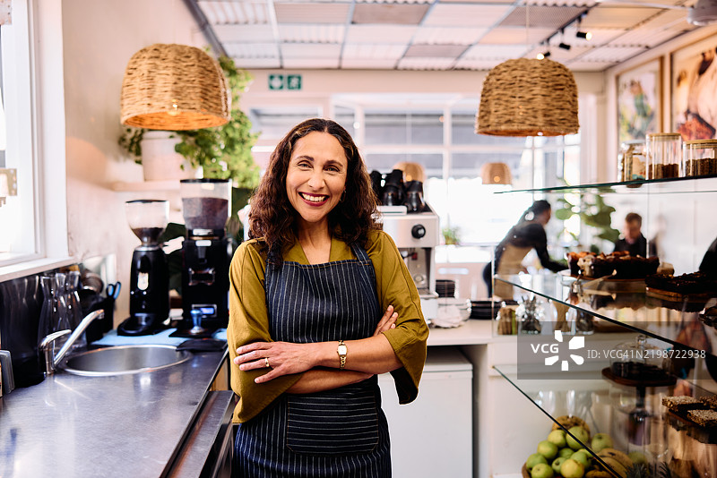 五十多岁快乐的女性企业主在咖啡馆工作，双臂交叉。图片素材