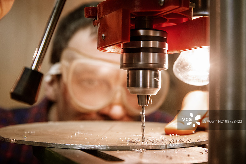 钻孔金属圆盘。工人在佩戴安全装备的情况下操作钻床。图片素材