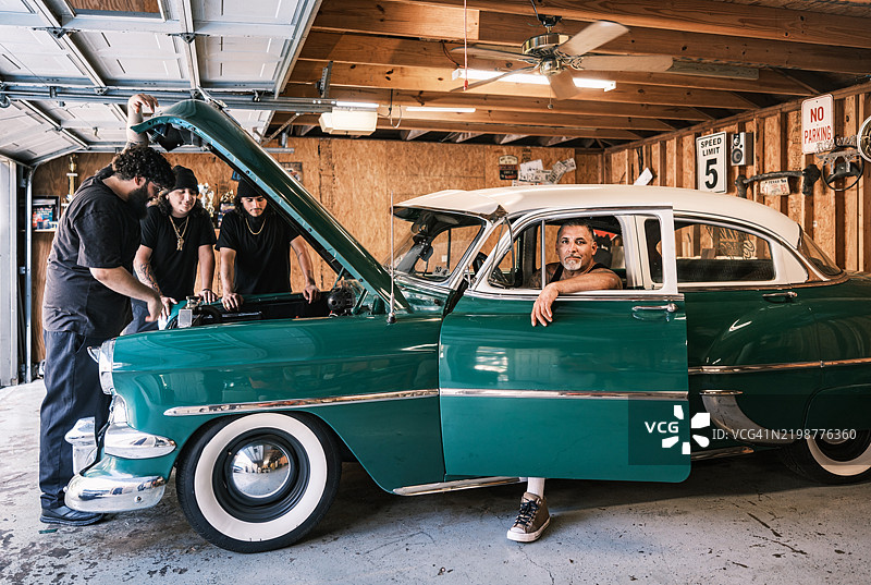 中年拉丁裔男性低骑车爱好者与他的三个儿子一起修理汽车图片素材