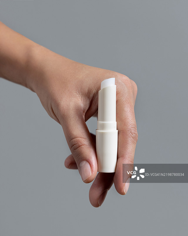 手握白色打开的润唇膏棒，背景为灰色特写，化妆品展示，留白空间图片素材