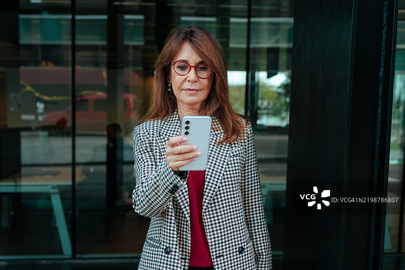 女商人在办公大楼前使用智能手机图片素材