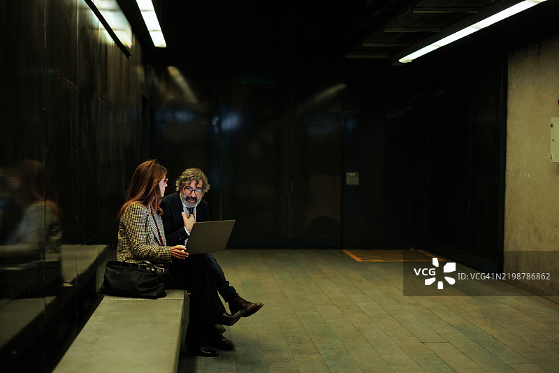 在昏暗的办公室走廊中使用笔记本电脑的商务人士图片素材