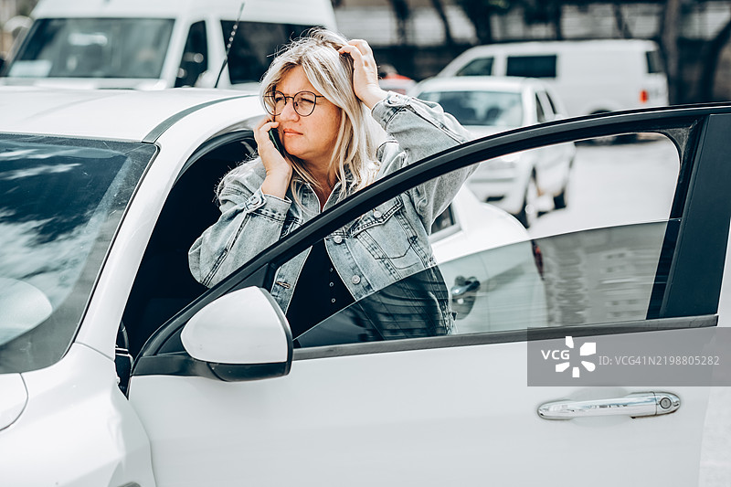 繁忙的城市生活：女性在下车时进行电话交谈。年轻女性从扣押停车场取车。女性司机在停车场使用手机。图片素材