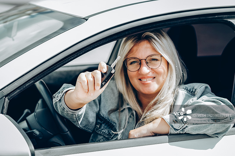 女人坐在车里手握钥匙，象征着新车拥有或驾驶执照的获得。图片素材