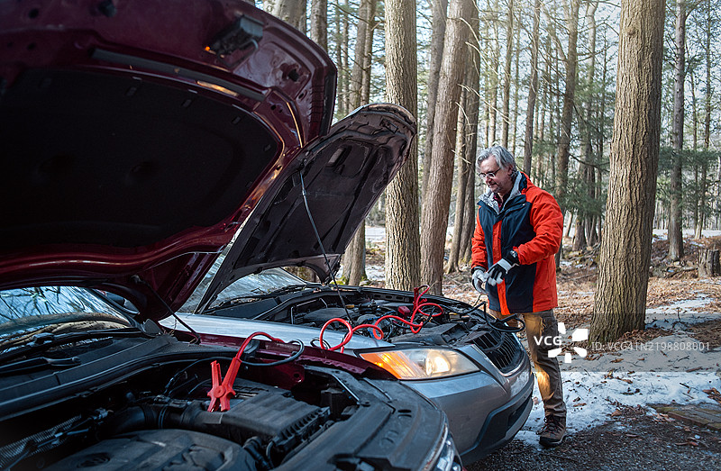 54岁男子在冬季森林中使用跳线电缆为没电的电池充电图片素材