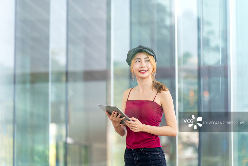 时尚年轻女性在现代玻璃建筑中使用平板电脑，透过玻璃拍摄。图片素材