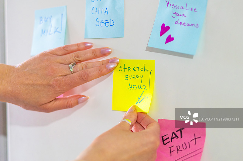 女人在冰箱上用便利贴规划她的一天。提醒便条帮助她全天保持高效和积极。图片素材