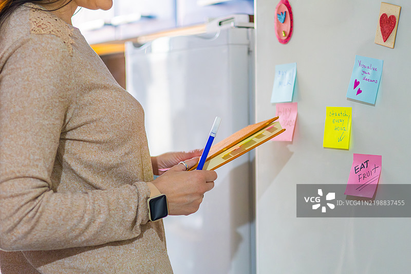 女人在冰箱上用便利贴规划她的一天。提醒便条帮助她全天保持高效和积极。图片素材