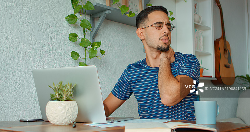 年轻男子因颈部疼痛而在笔记本电脑上工作。图片素材