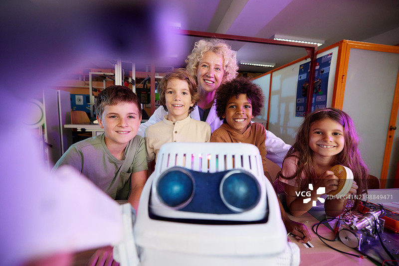 快乐的小科学家们与他们的老师和机器人在实验室里自拍。图片素材