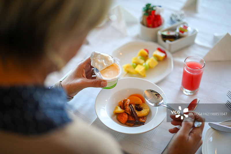 早餐桌上手部特写，旁边有一碗水果和酸奶图片素材