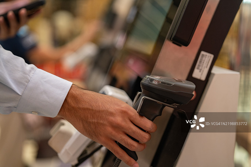 在超市购物的男子正在付款。照片中有顾客在商店内购物。此人正在使用非接触式支付。图片素材