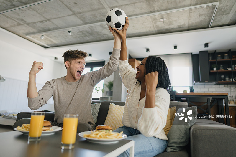 兴奋的情侣在家观看比赛时欢呼并举着足球图片素材