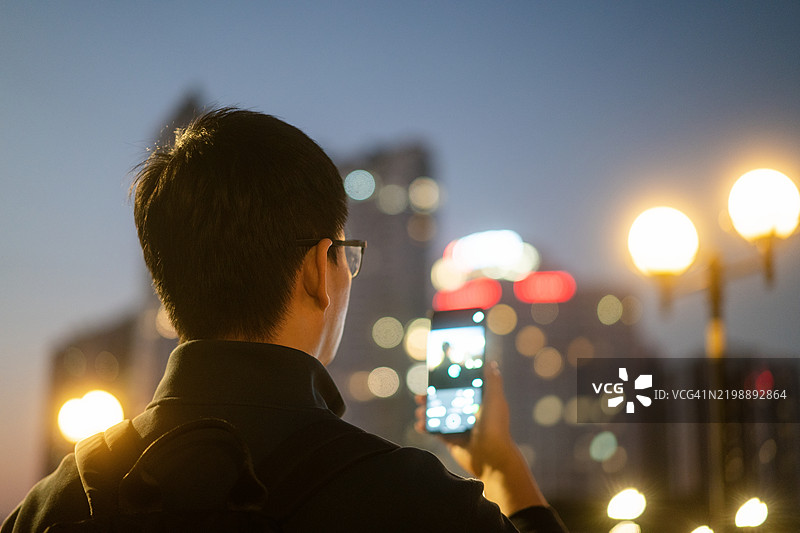 亚洲男子在夜晚的城市中使用智能手机图片素材