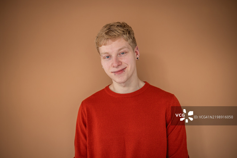 自信的年轻男子，金发和穿孔，微笑着在现代室内环境中享受闲暇时光。图片素材