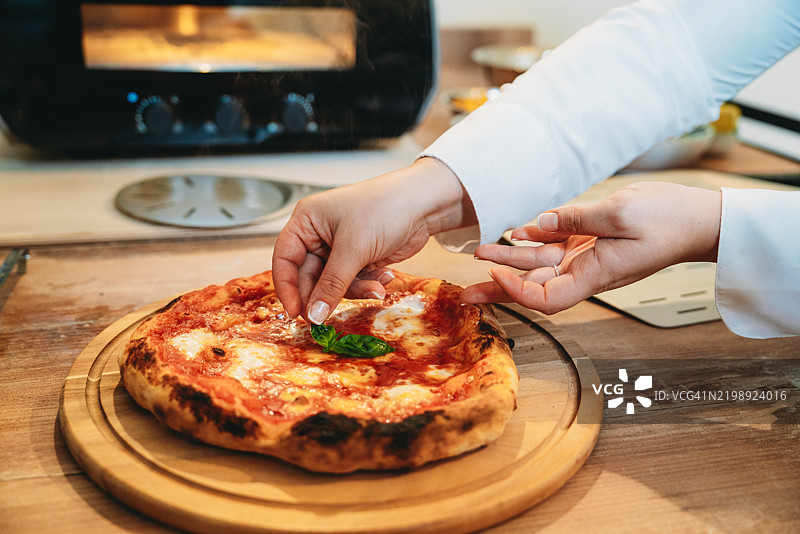 厨师在刚出炉的玛格丽塔披萨上添加新鲜的罗勒叶图片素材