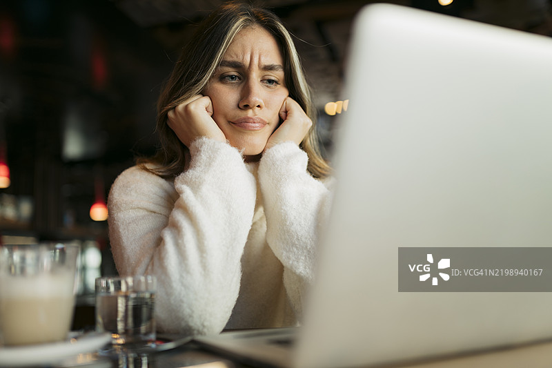 年轻女性在咖啡馆里对着笔记本电脑显得很烦恼图片素材