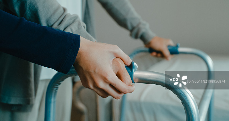 年轻的亚洲护士在床上帮助一位老年女性使用助行器，家庭护理和老年人支持。图片素材