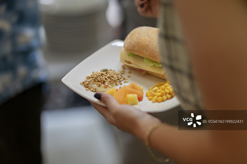 女人手持一个装有三明治、酸奶、水果和玉米的盘子图片素材