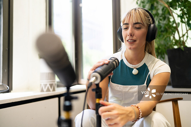 女性在明亮的工作室环境中使用专业麦克风录制播客图片素材