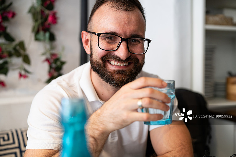 微笑的戴眼镜男子在轻松的环境中手持一杯水的肖像图片素材