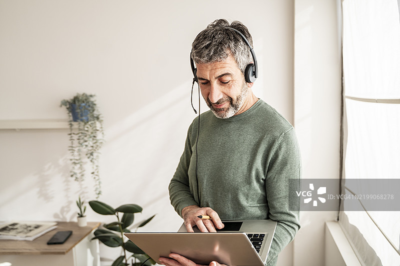 专注的成熟商务人士戴着耳机，使用笔记本电脑进行在线会议或视频会议，在家中的办公室远程工作图片素材