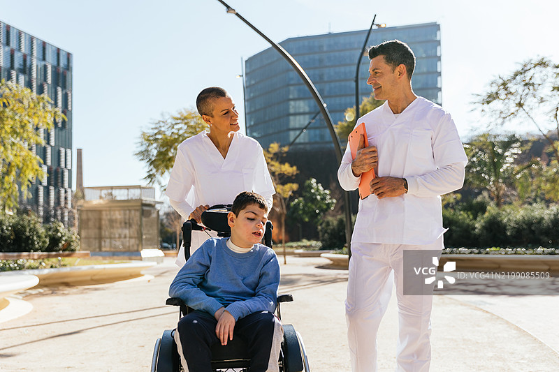 医疗团队在户外推着坐在轮椅上的孩子图片素材