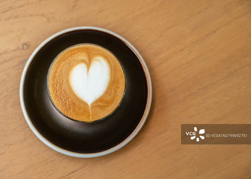 一杯拿铁咖啡放在木桌上。图片素材