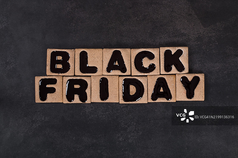 黑色星期五。方形饼干夹着黑色果酱，形状为“黑色星期五”字样。深色背景。图片素材