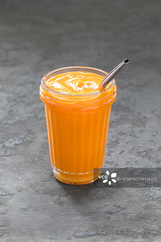 玻璃杯中的南瓜奶昔配金属吸管。深灰色背景图片素材