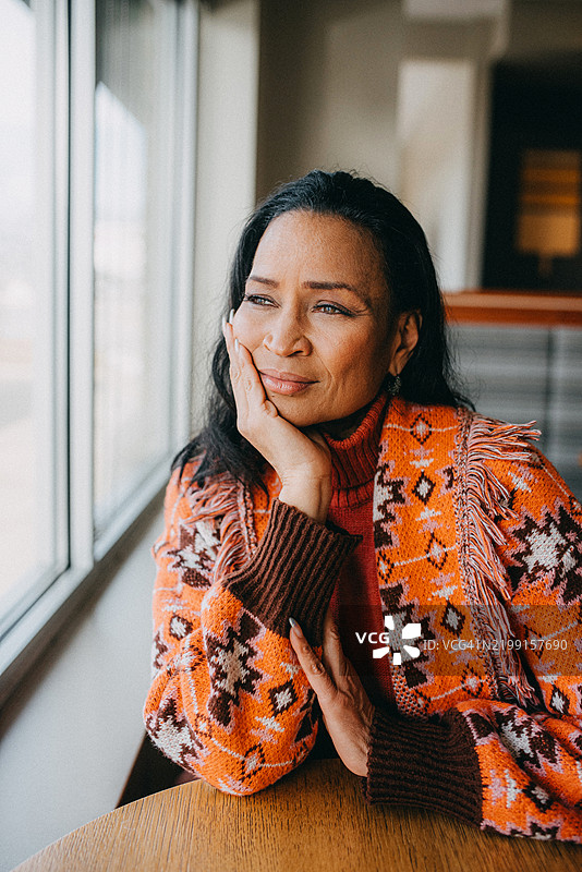 一位女性沉思地望着窗外，手下巴托着。图片素材