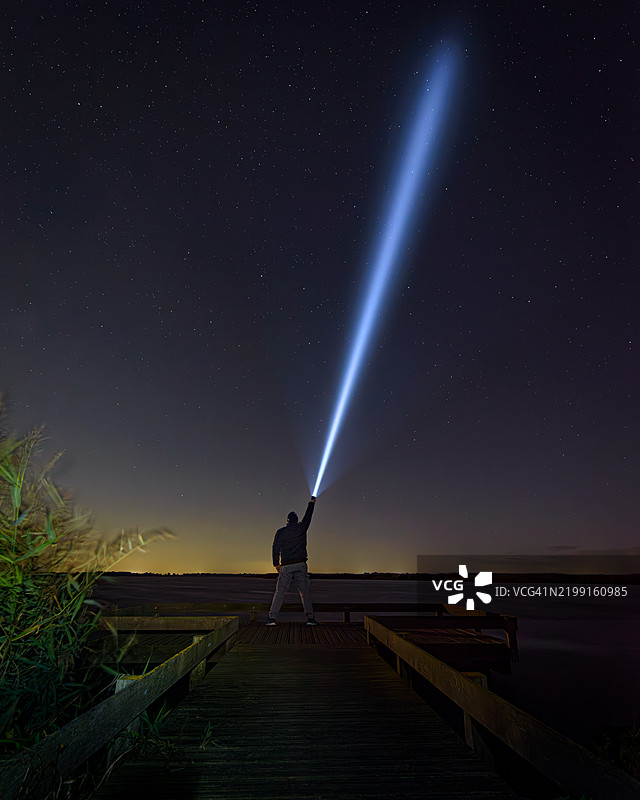 夜晚，男子背对天空手持手电筒。图片素材