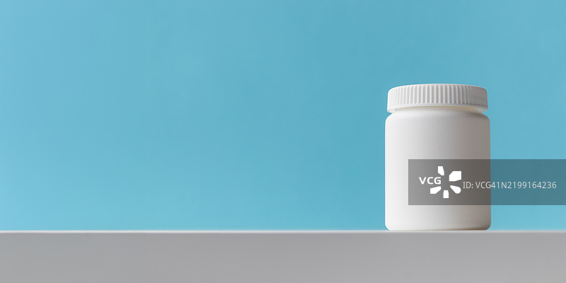蓝色背景上的白色塑料药瓶，留有空白空间，包含药物和健康概念，瓶中装有药丸或维生素，高质量的照片展示横幅图片素材