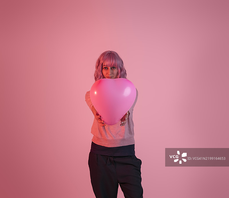 女人在工作室里手持粉色心形气球，周围有粉色灯光，情人节气氛。图片素材