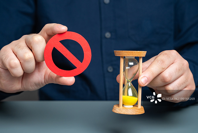 一名男子手持红色禁止标志和沙漏，时间紧迫，截止日期临近，重要的禁令必须毫不延迟地遵守，临时限制仅限于有限时间。图片素材